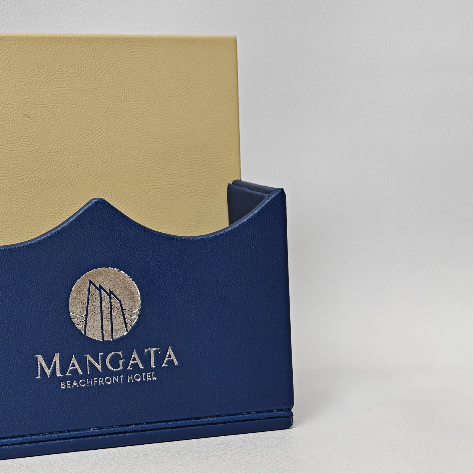 Close-up of a silver foil logo on blue pebbled leather with a decorative wave-shaped top edge.