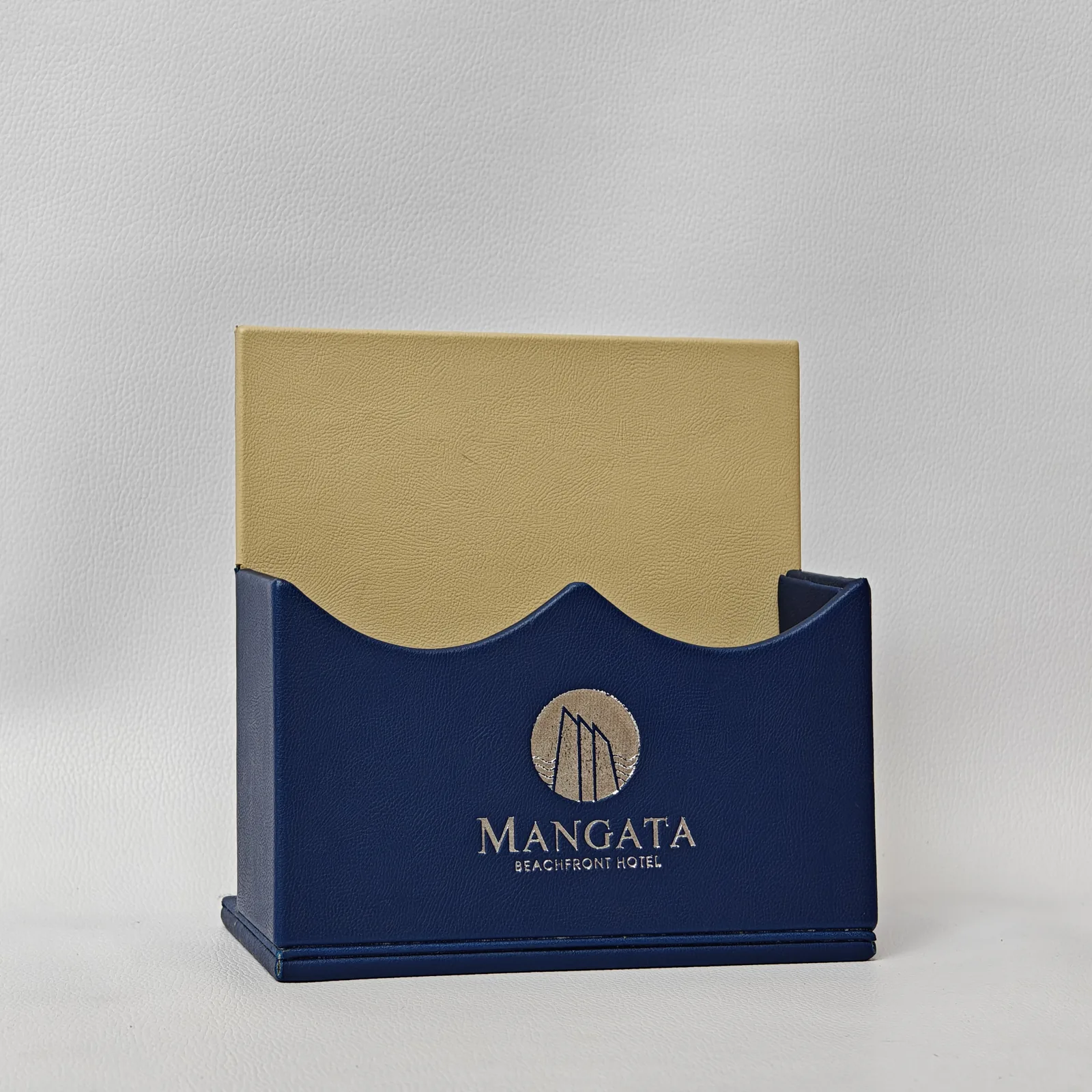 Front view of a blue leather desk organizer with a tan back panel and a silver embossed circular logo.